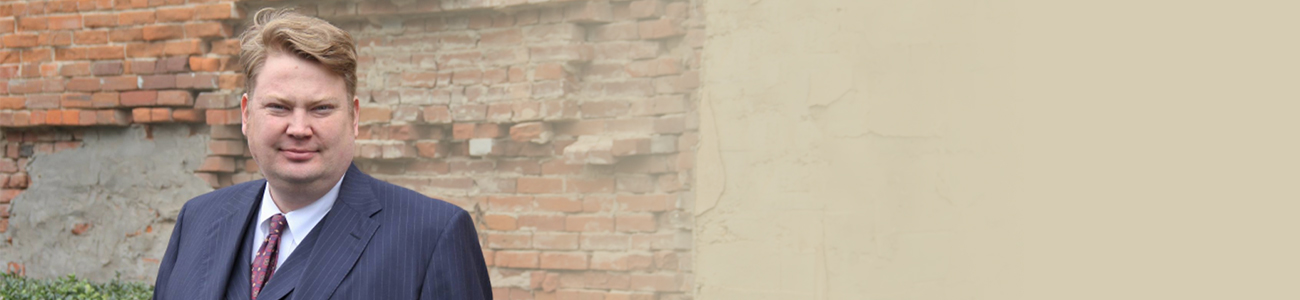Micah Belden with a brick wall and a shrub in the background.